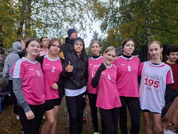 Grupa uczennic i uczniów w sportowych strojach pozuje podczas zawodów biegowych na świeżym powietrzu.