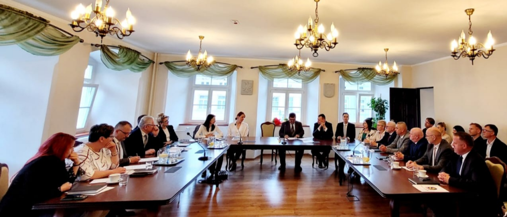 Sala Rajców Urzędu Miejskiego w Leśnej podczas sesji rady miejskiej z udziałem radnych siedzących przy stołach konferencyjnych.